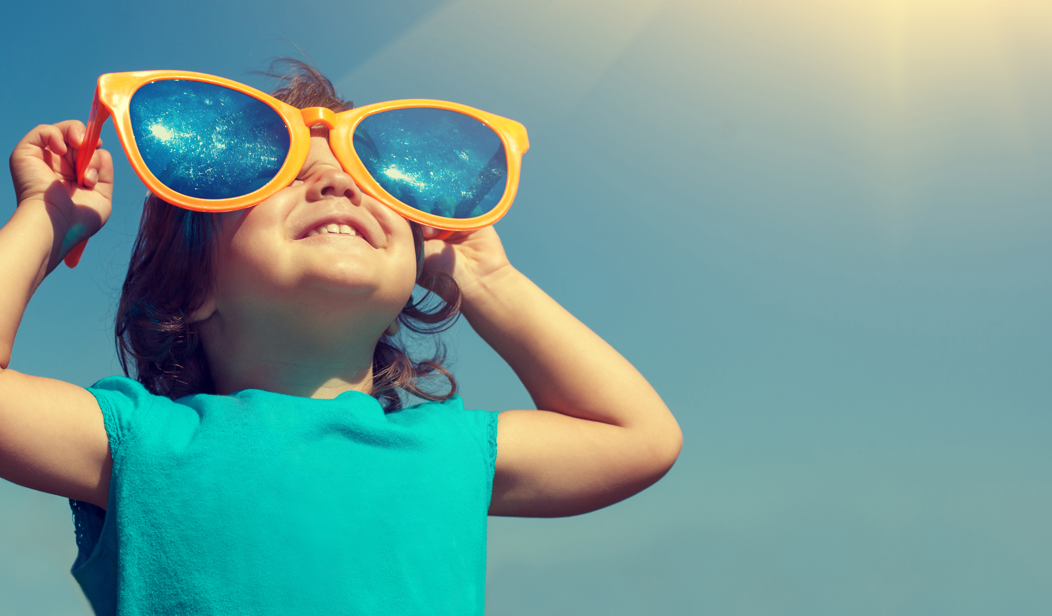 child looking through sunglasses, blue sky with sun shining in back ground