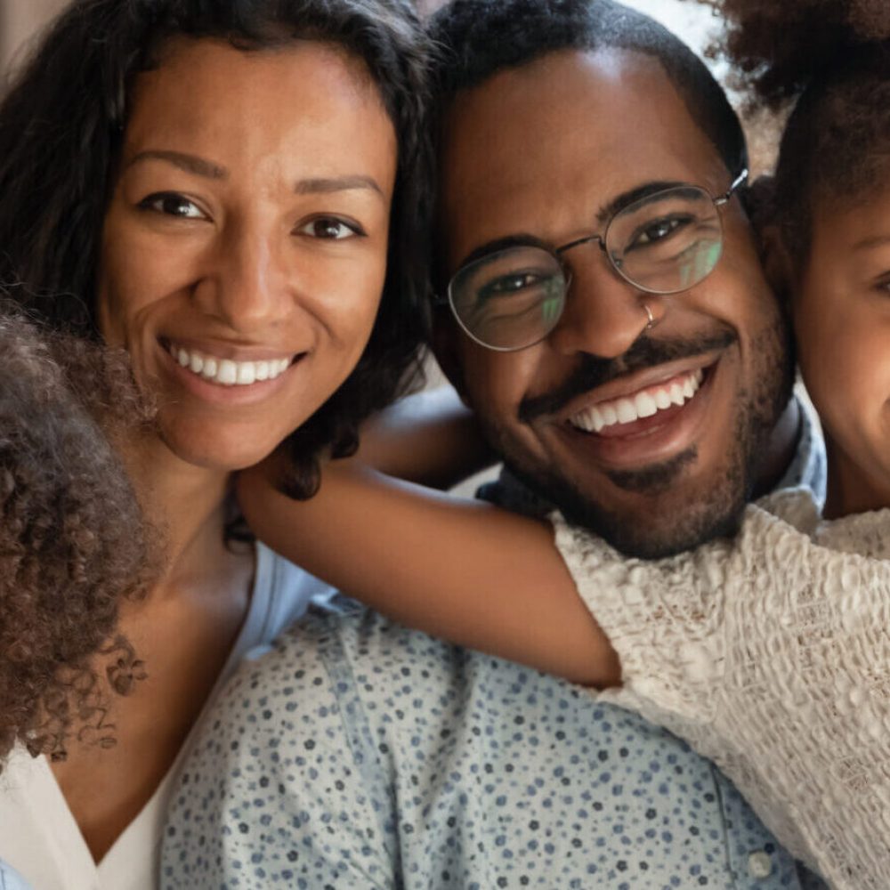 Portrait of happy african ethnicity family bonding with small kids on comfortable sofa. Cheerful loving devoted mixed race couple cuddling cute little children siblings, relaxing at weekend at home.