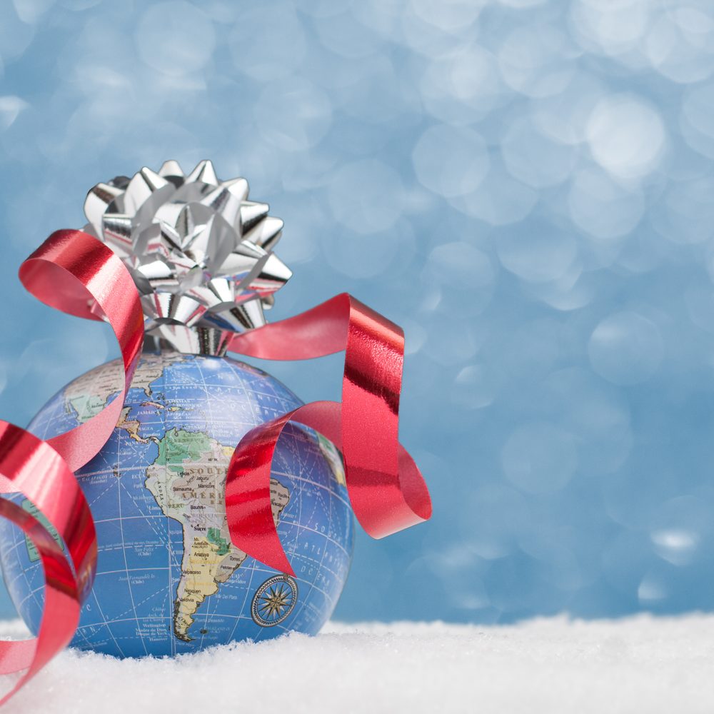World globe sits in snow on blue twinkle background with ribbon and bow