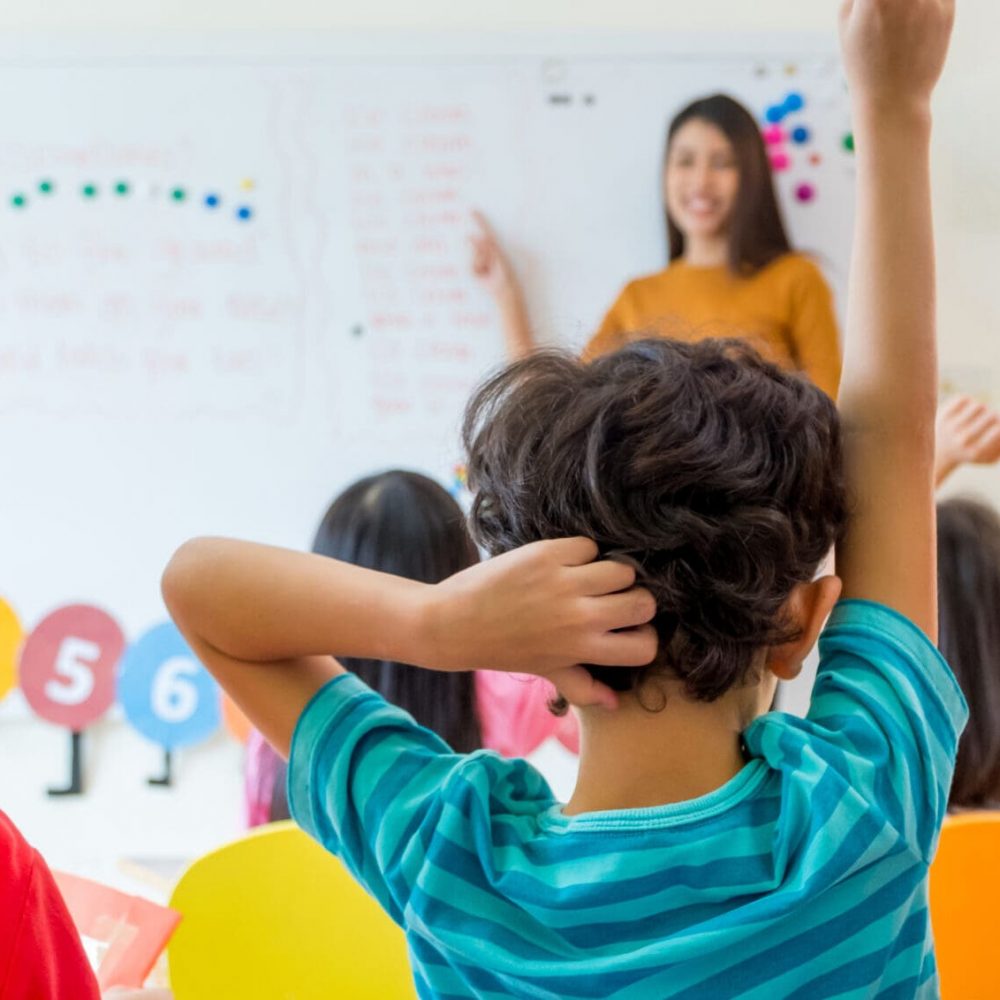 Preschool kid raise arm up to answer teacher question on whiteboard in classroom,Kindergarten education concept school readiness
