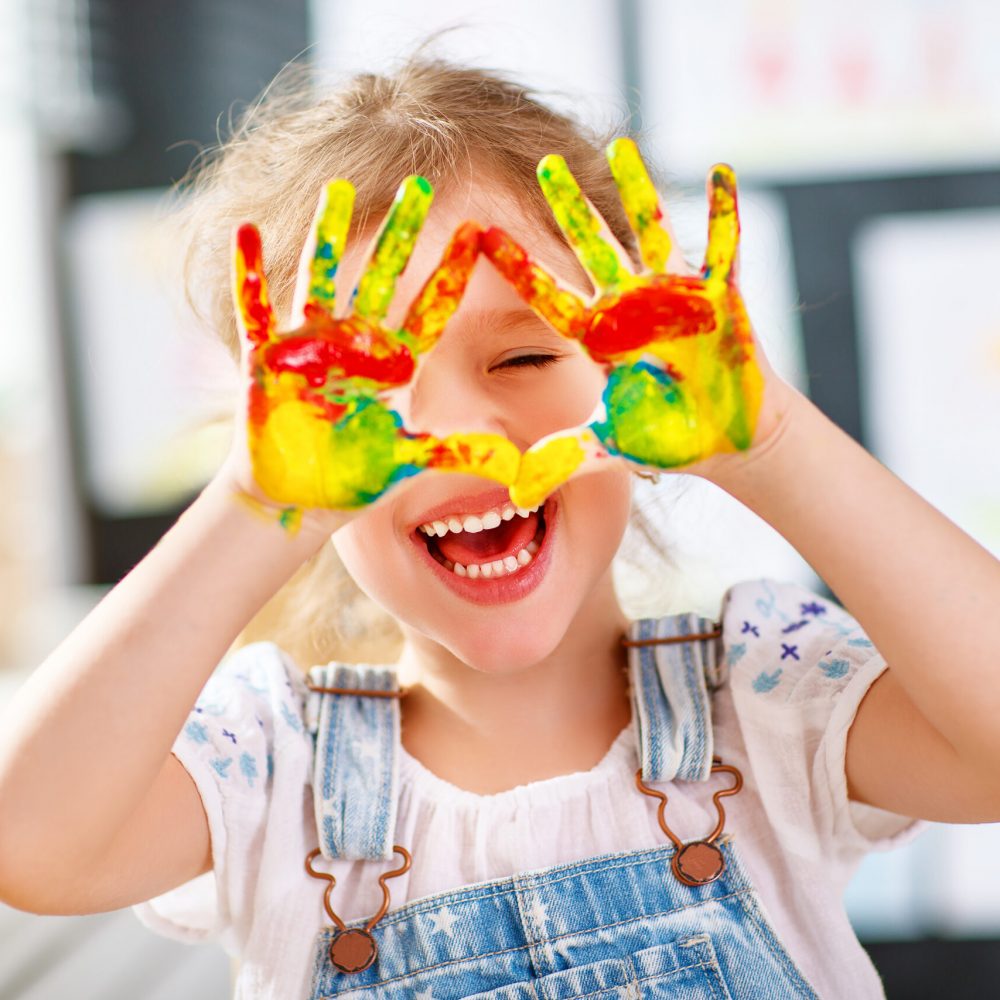happy funny child girl draws laughing shows hands dirty with paint